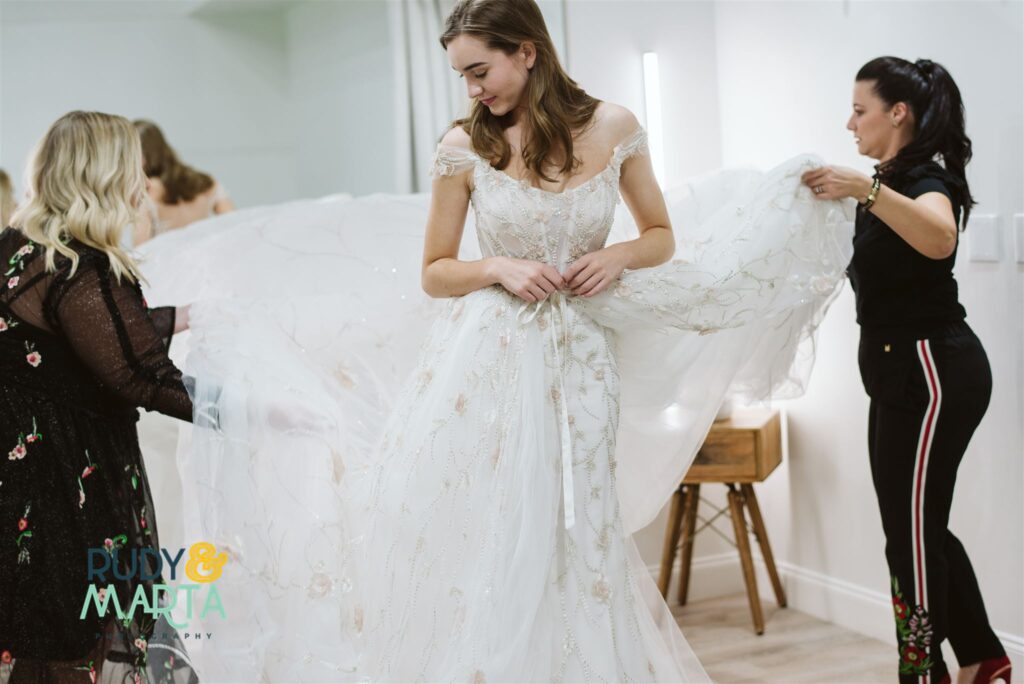 bridal shop employees holding train of lace wedding dress to show bride - bridal finery orlando wedding gowns