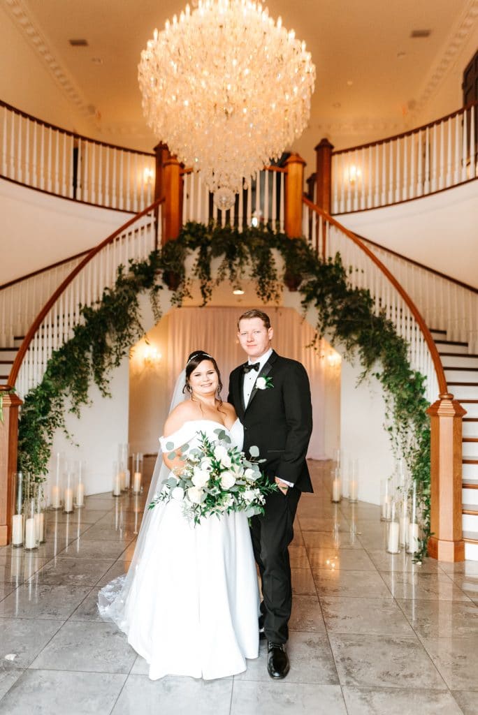 CDC Floral - bride & groom standing in front of double staircase adorned with greens