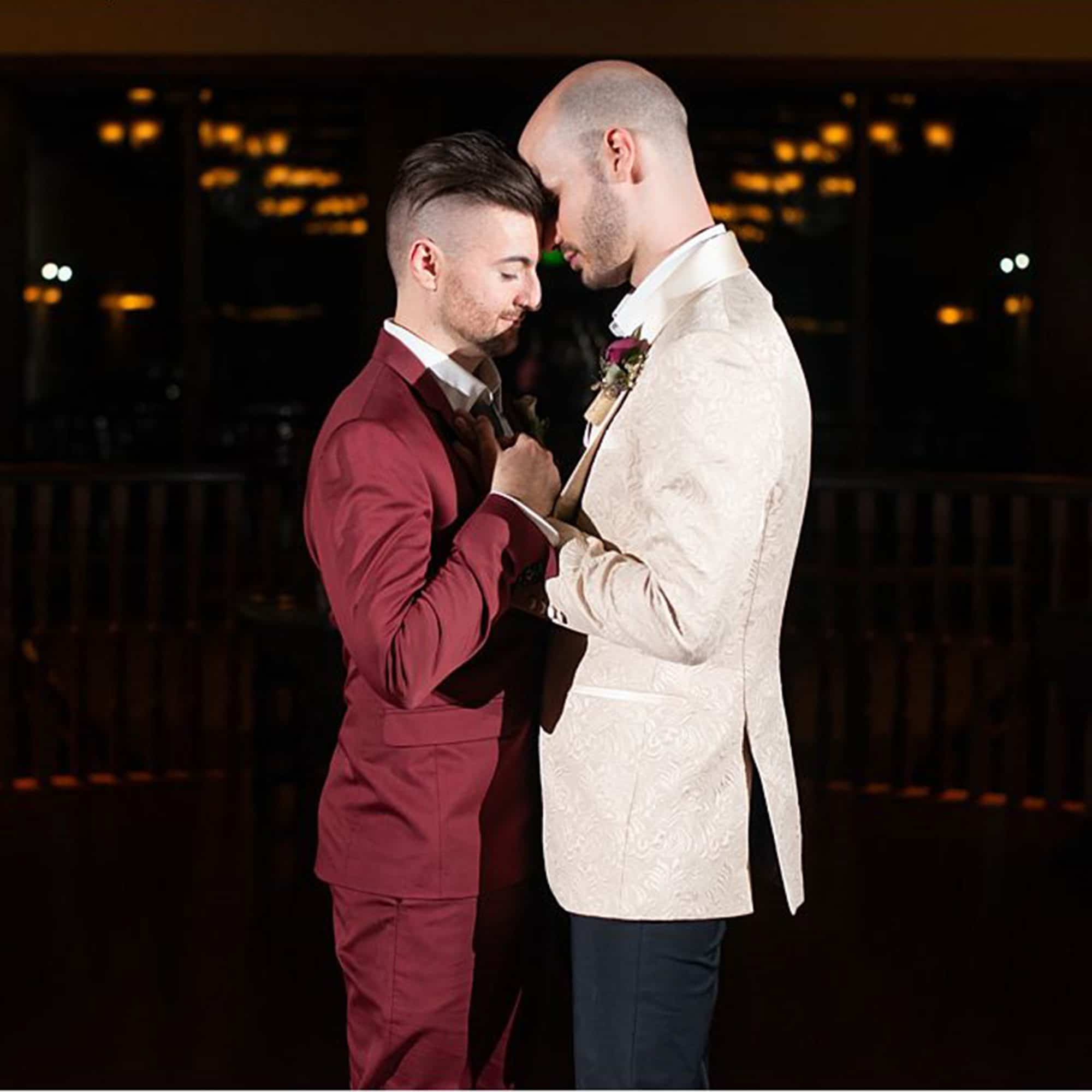 Two grooms holding hands with foreheads pressed together