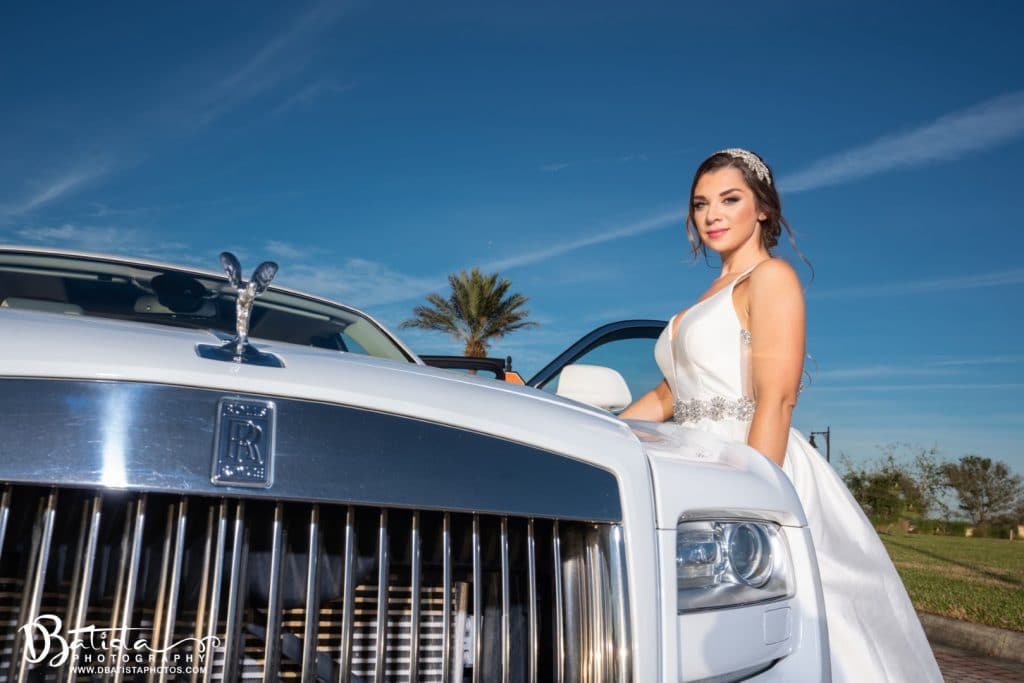 Exotic-Limo-Orlando-Bride standing next to white Rolls Royce Ghost with blue sky