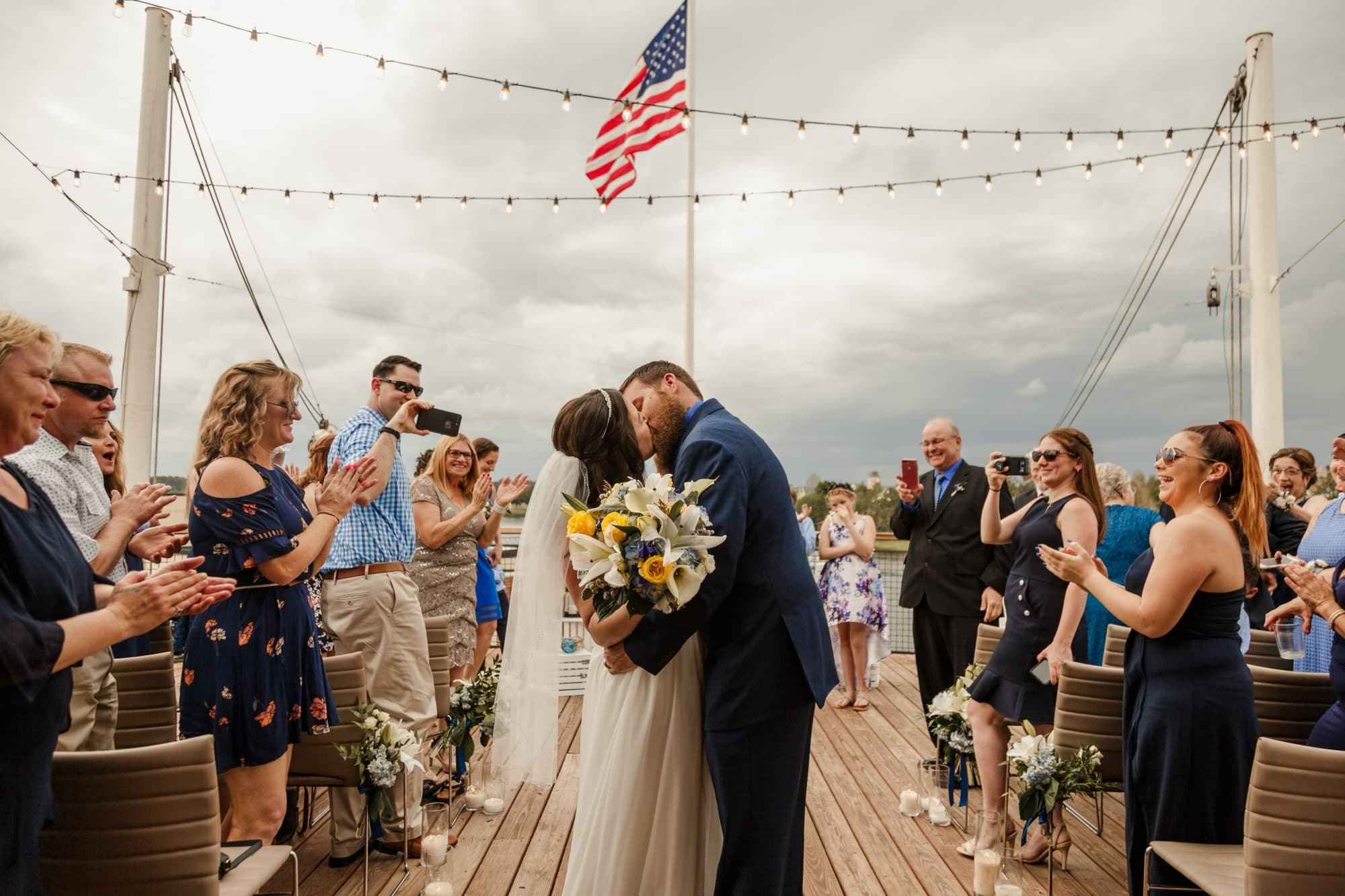 For the Love of Events - Newlyweds kissing on dock in front of wedding guests