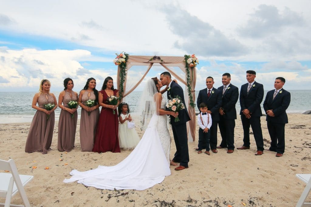 Live-Love-Laugh-Events-Bride and Groom kissing on the beach with bridal party in the background