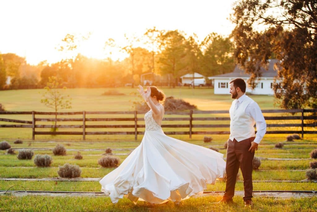 Live-Love-Laugh-Events-Bride twirling in wedding dress outside at sunset with groom watching