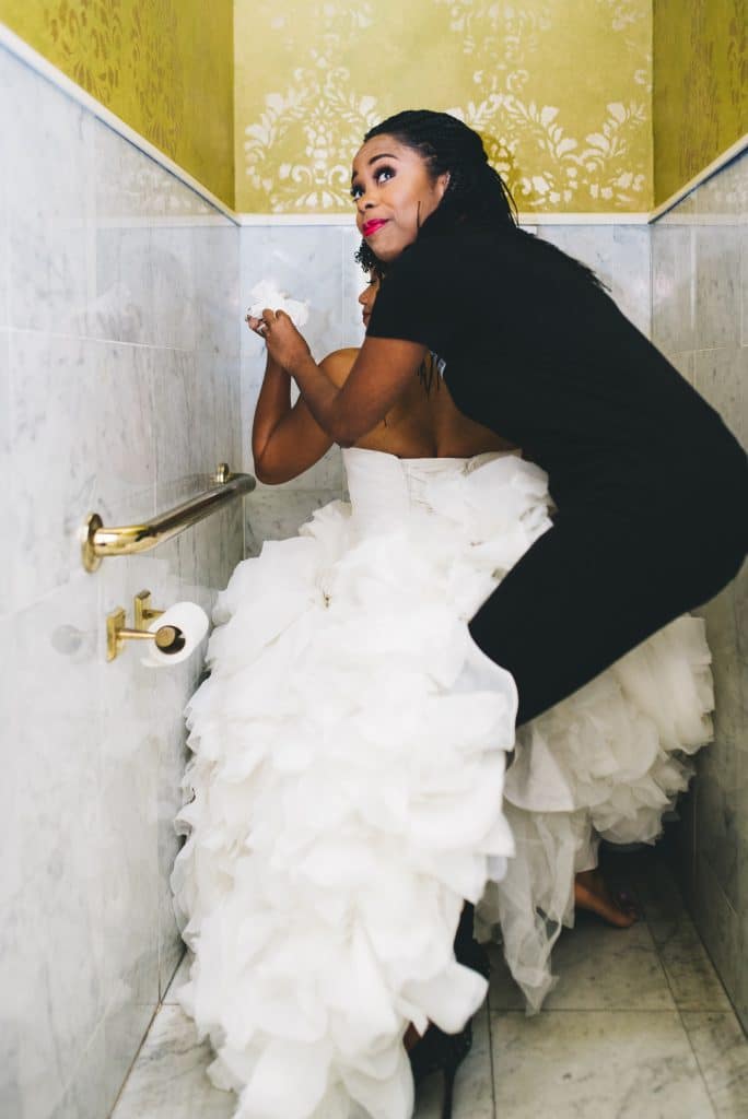 event planner helping bride with gown in bathroom