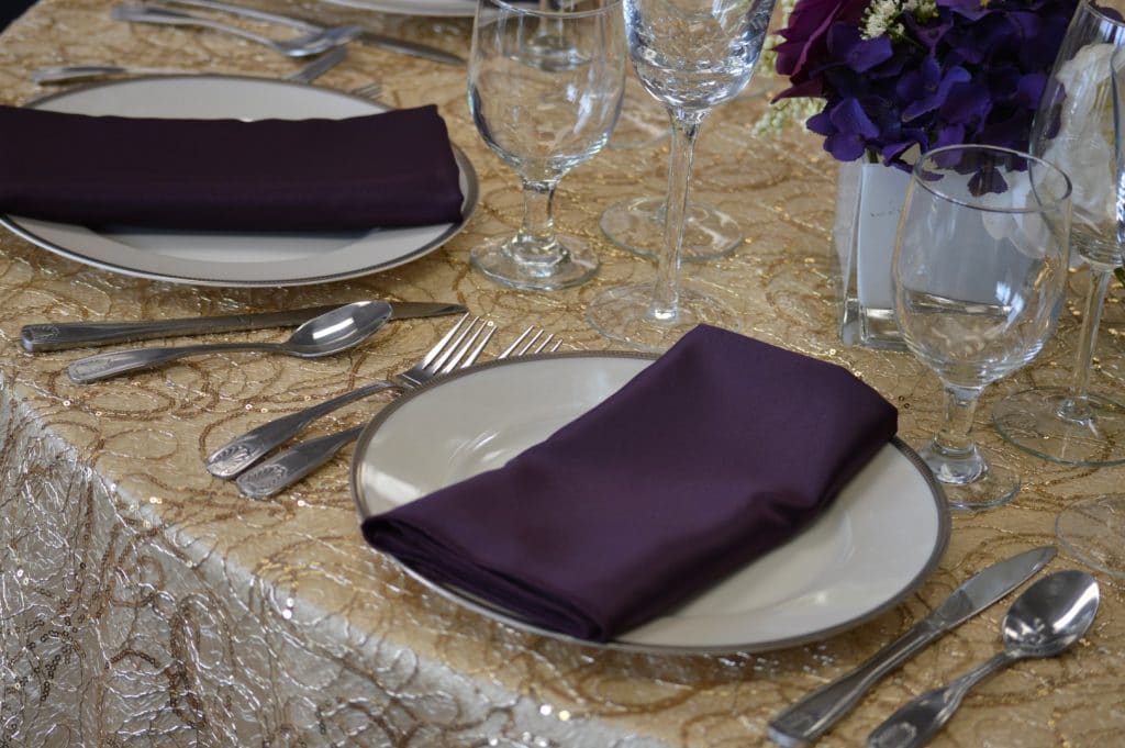 Connie-Duglin-Linen-Creme and gold sequin linen with dark purple napkin and silver rimmed dinner plate