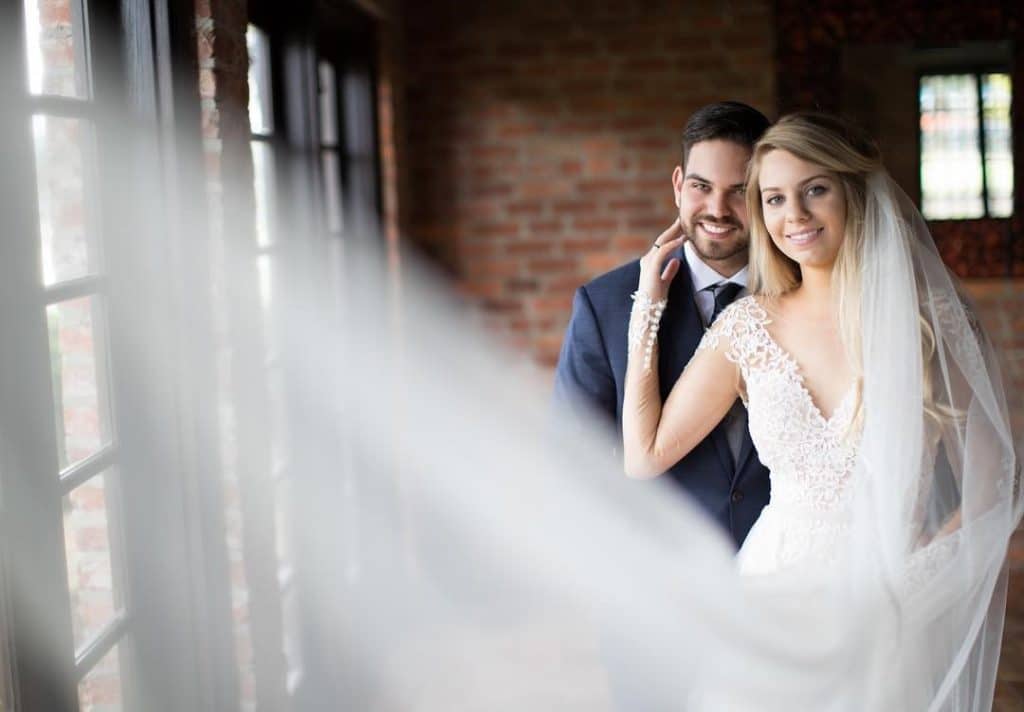 As-You-Wish-Bride touching Grooms face while smiling next to french doors