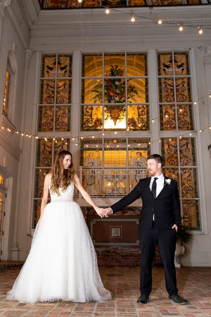 Photolicity - bride and groom holding hands in front of giant stained glass window