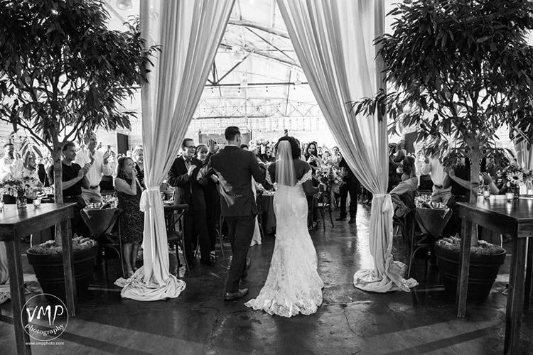 1010 West - bride and groom walking through curtains inside airplane hangar turned reception venue
