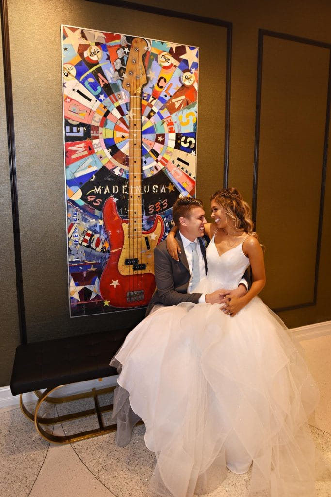 bride and groom posing next to colorful artwork of guitar.