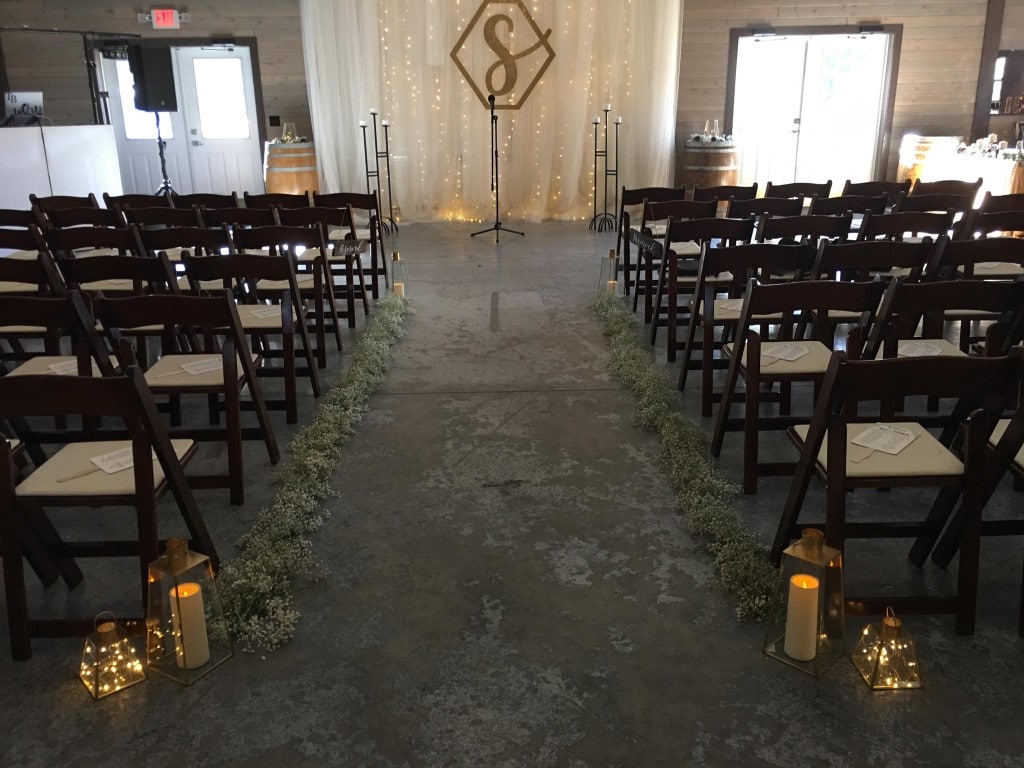 Perfect-Day-Productions- Indoor wedding ceremony with candles lighting aisle and wooden monogram on backdrop