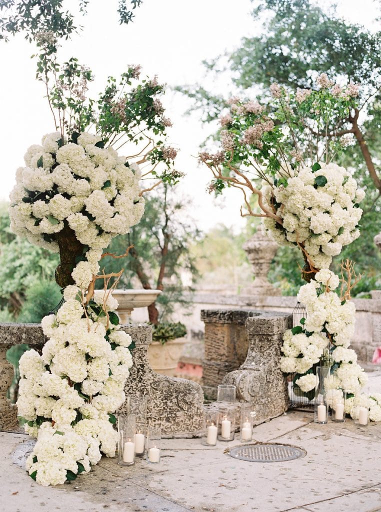 wedding arch with large white floral arrangements entwined into wooden reed boughs