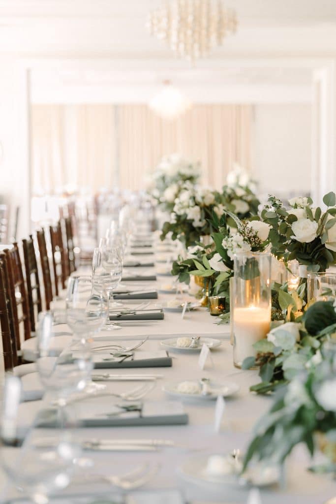 long wedding reception table set with white linens, white candles and white floral centerpieces