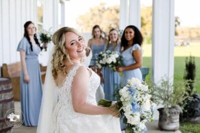 bride looking over her shoulder and smiling at camera with bridesmaids in blue dresses in the background