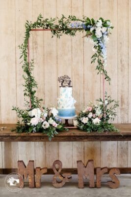blue and white wedding cake surrounded in floral bouquets and garland