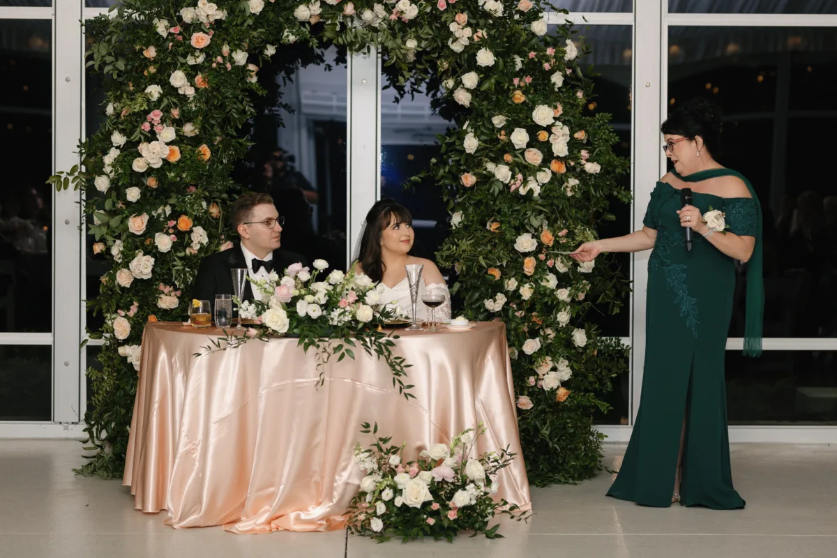 Romantic garden-style wedding sweetheart table with blush and ivory roses beneath a lush floral arch