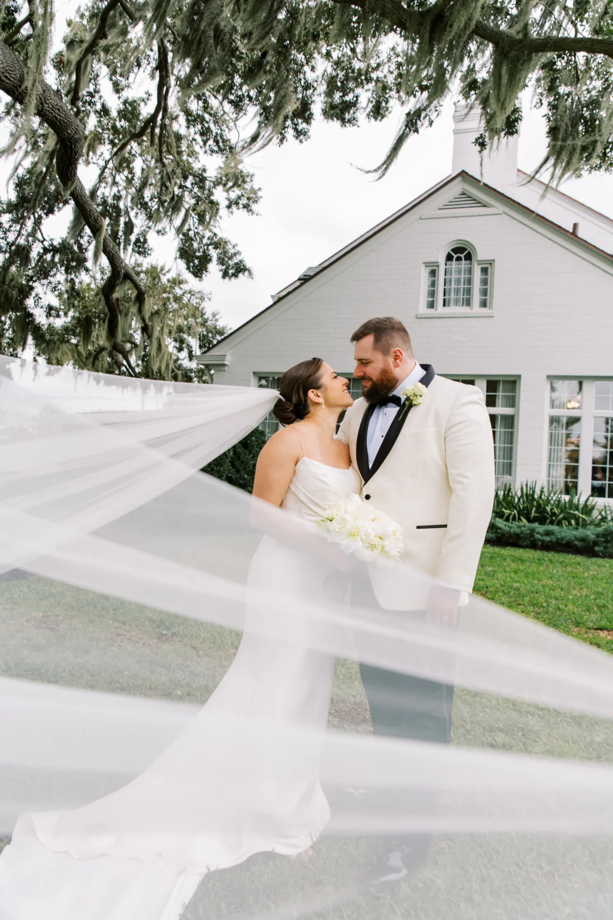 bride and groom under mossy oak tree with white barn in background
