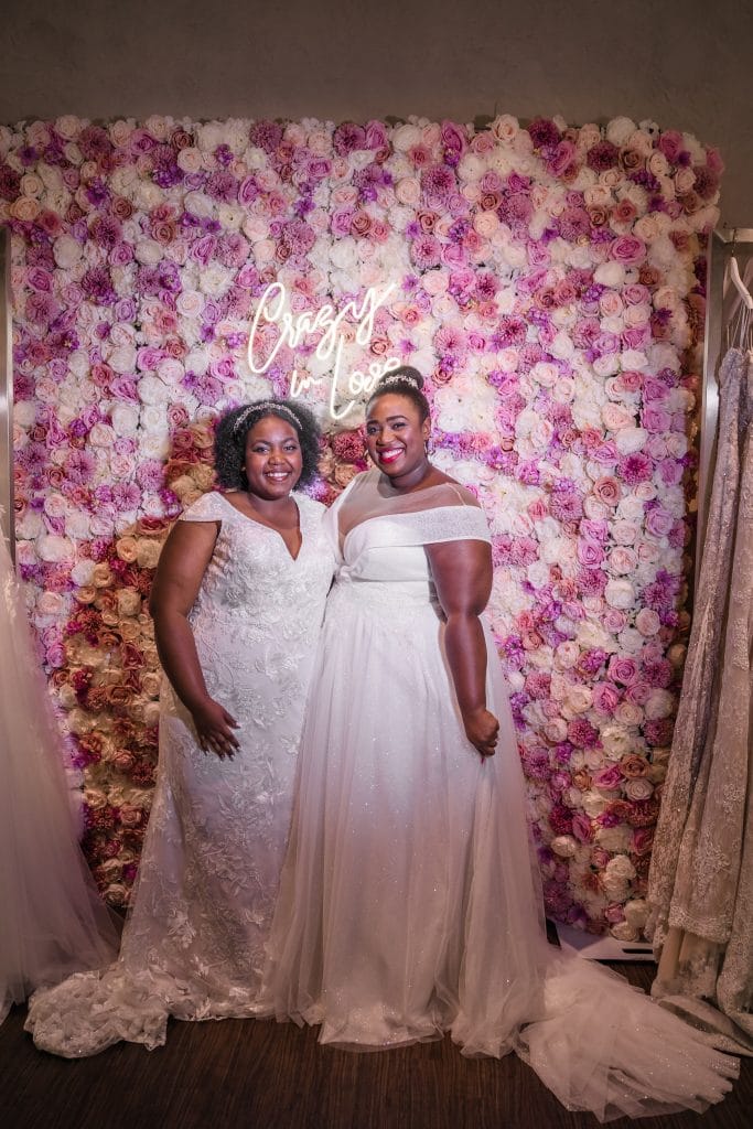 two brides in front of pink flower wall