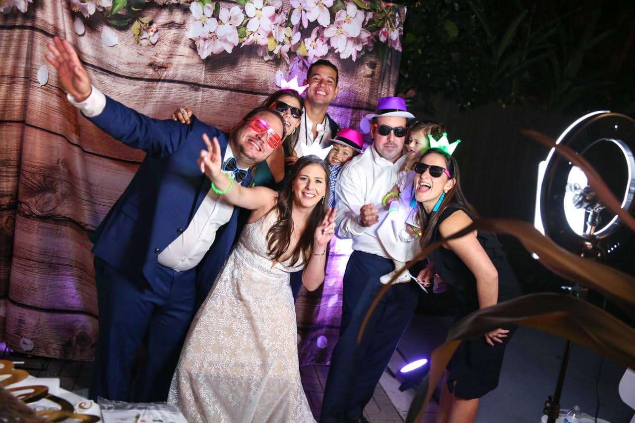 Live Happy Studio - wedding guests wearing hats & glasses in front of a backdrop