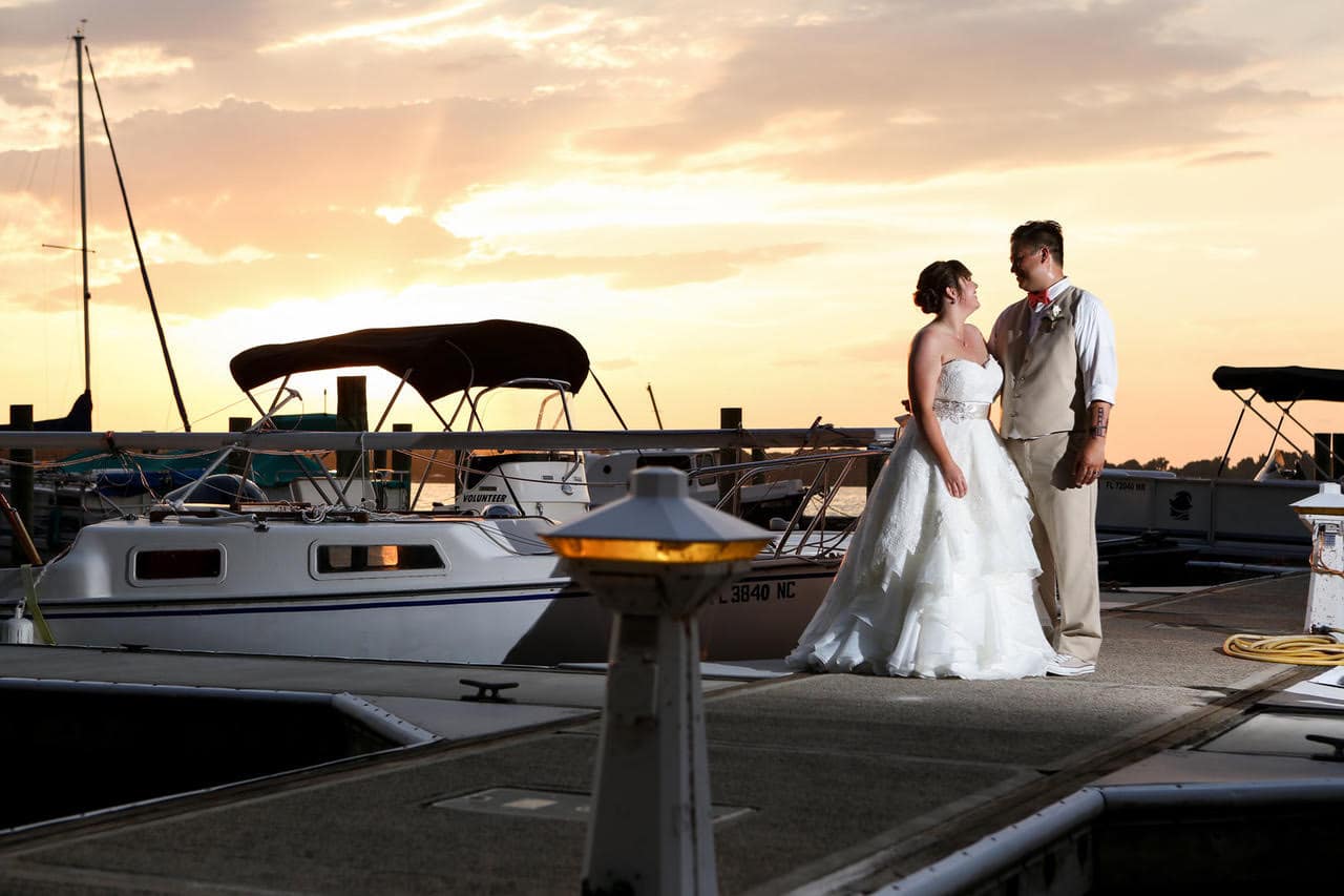 Live Happy Studio - bride & groom standing on a boat dock at sunset