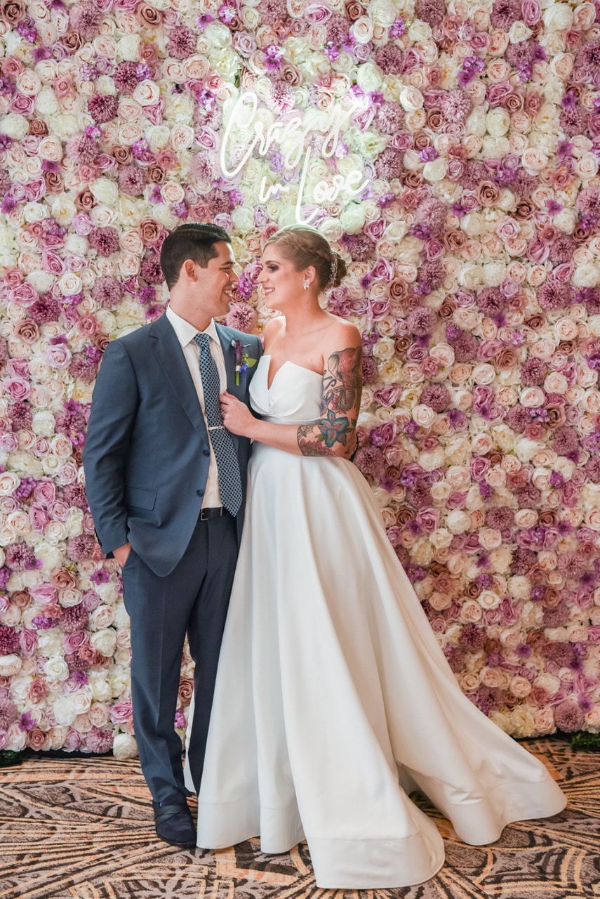 bride and groom standing in front of orlando flower walls with lighted crazy in love sign