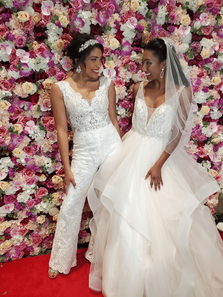 two brides standing in front of multi-colored flower wall