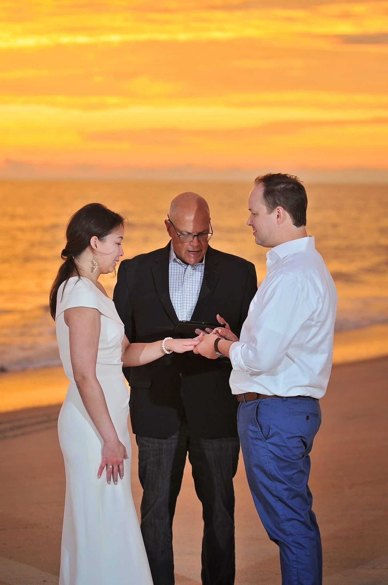 Pastor Mike standing on the beach at sunset with bride and groom