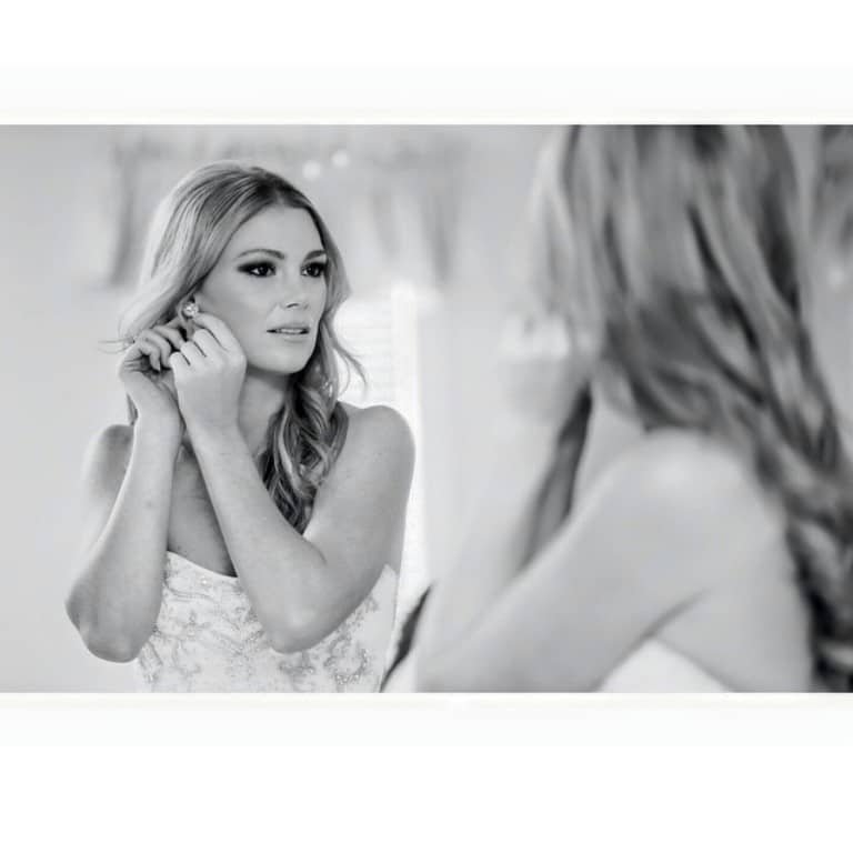 black and white photo of bride putting on earring with her hair and make-up styling by Jazz It Up Artistry