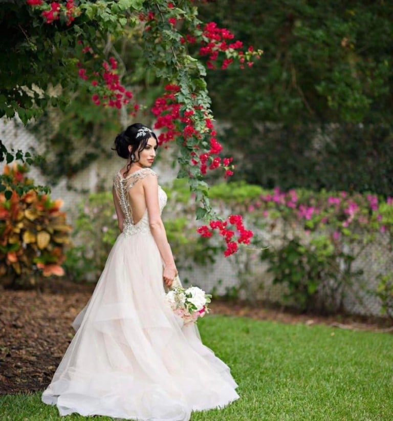 bride styled by Jazz It Up Artistry with tiara in her hair standing in a garden of flowers