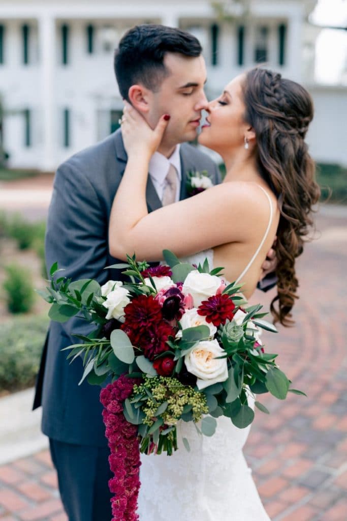 bride with braided hair styled by Jazz It Up Artistry and groom kissing on brick walkway