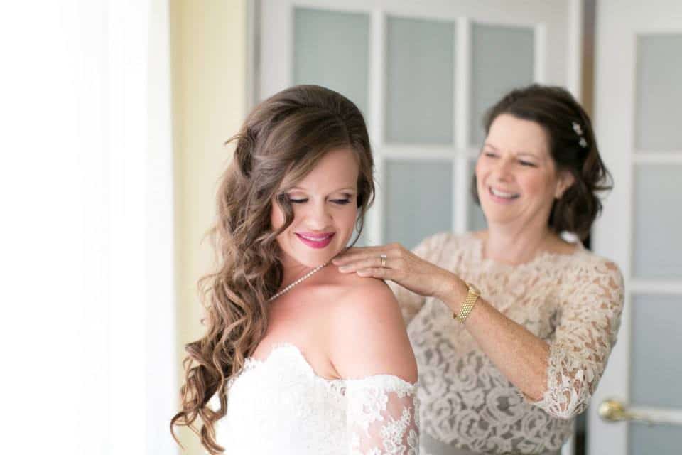 mother of bride helping put on wedding necklace with bride's make-up and hair styled by Jazz It Up Artistry