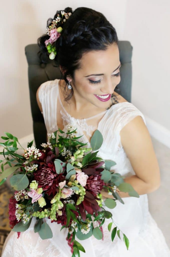 Honeywood Photography bride with bouquet of burgandy, pink flowers and greenery that match brides floral spray in her hair