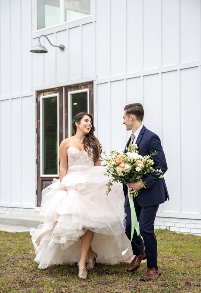 Honeywood Photography photo of bride and groom holding bride's bouquet walking and laughing together against a large white building