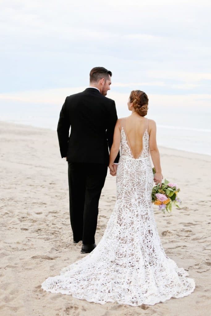Honeywood Photography photo of bride with a lace train and groom walking down the beach.