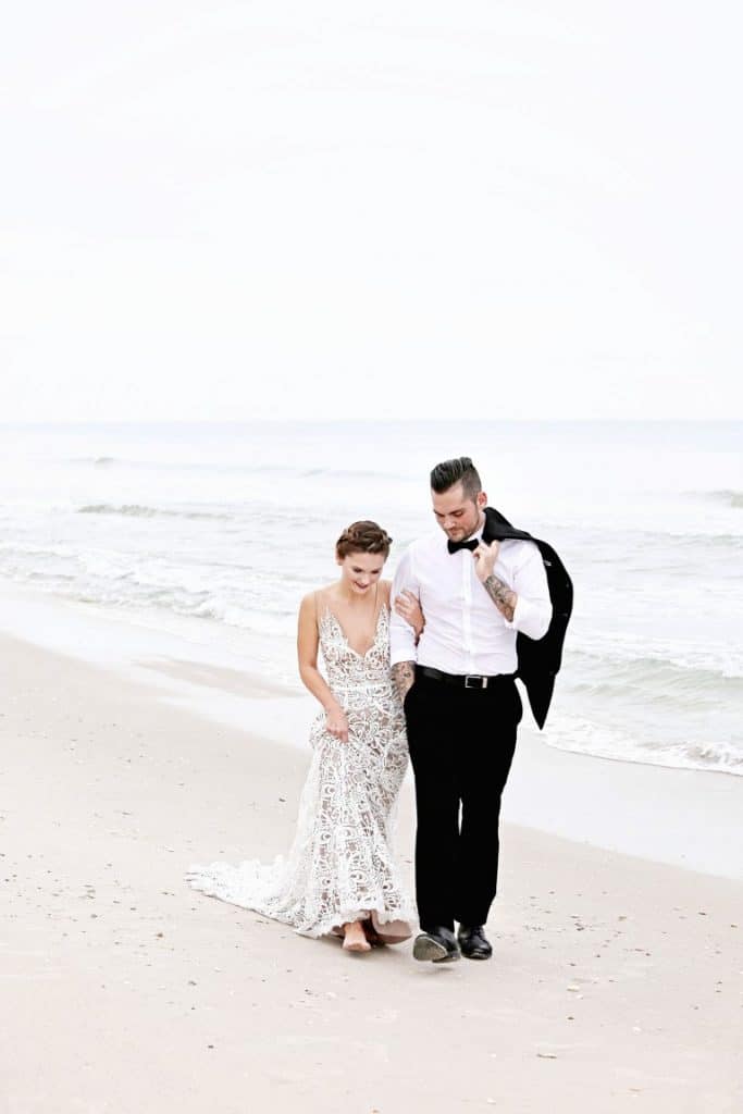 Honeywood Photography photo of a bride and groom with his tuxedo jacket over his shoulder walking on the beach