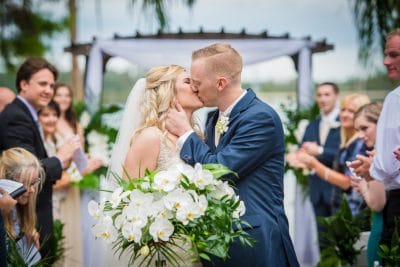 bride and groom kissing, large white floral bouquet, outdoors, wedding guests clapping, Sonacity Photography, Orlando, FL