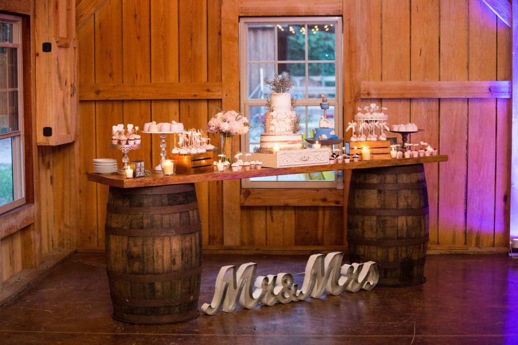 wedding cake table on wood barrels with Mr. and Mrs. sign in front of it by Foodie Catering