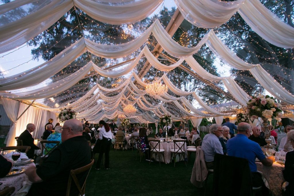 beautiful outdoor wedding reception with lights, drapery, and guests eating at their tables by Foodie Catering