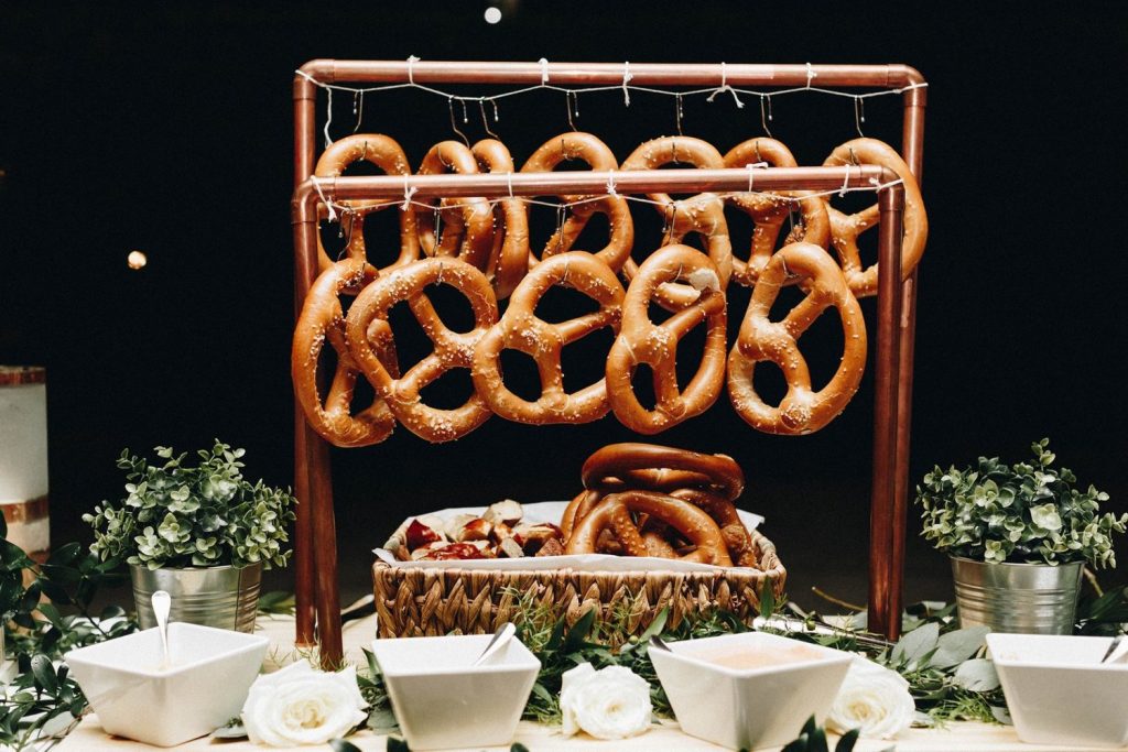large pretzels hanging on display at wedding reception, with dipping sauces nearby by Foodie Catering