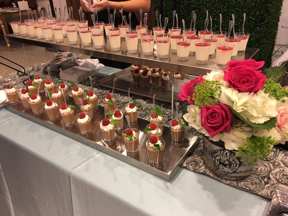 large table filled with individual desserts and flowers for decorations