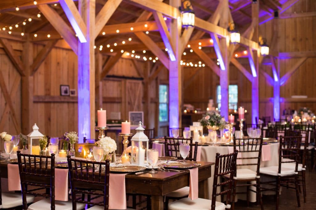 indoor wedding reception with beautiful lighting, wood interior, purple uplights, and tables set by Foodie Catering