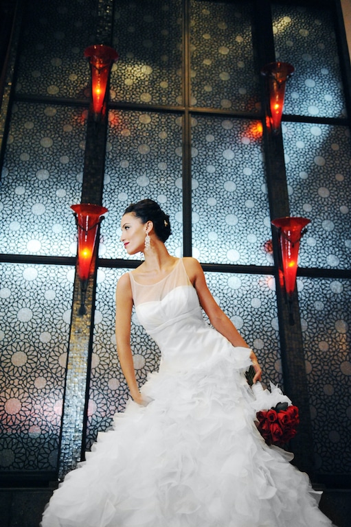 Beauté Spécialé Bride standing in front of wall with red lights holding roses