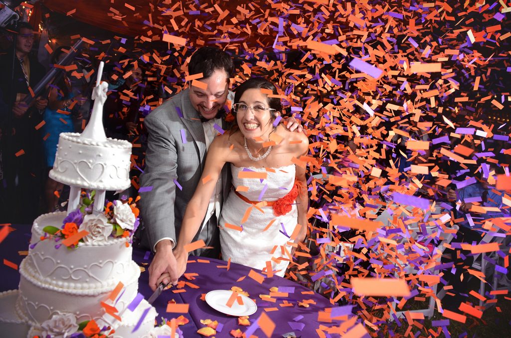 Jennifer Juniper Photography - Bride and groom cutting cake with bright confetti falling
