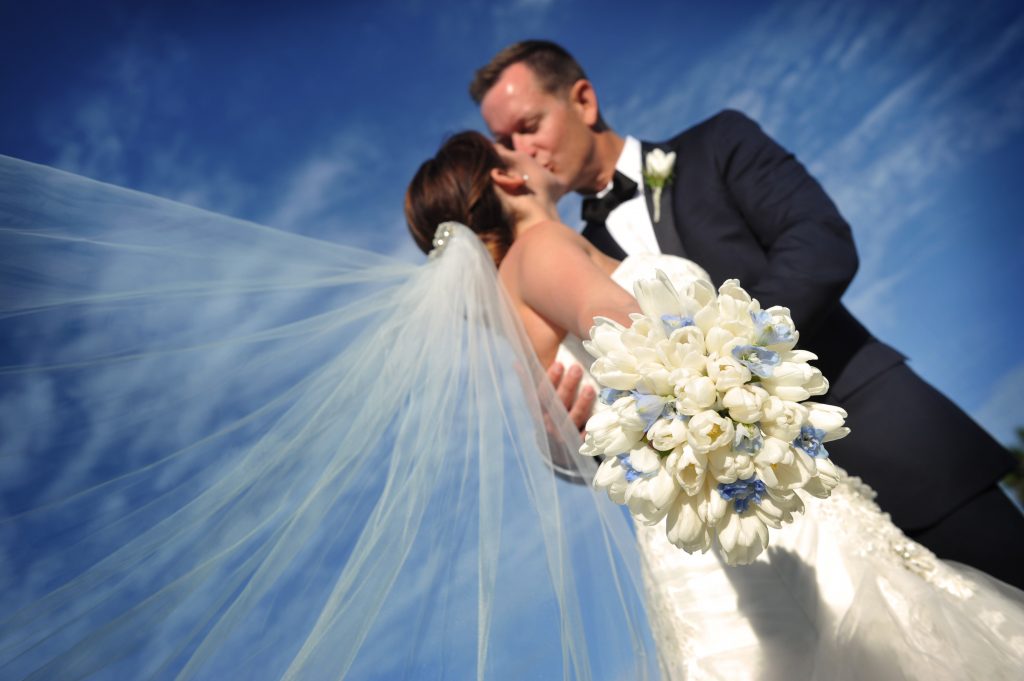 Jennifer Juniper Photography - Dutch angle of bride and groom kissing with blue sky background