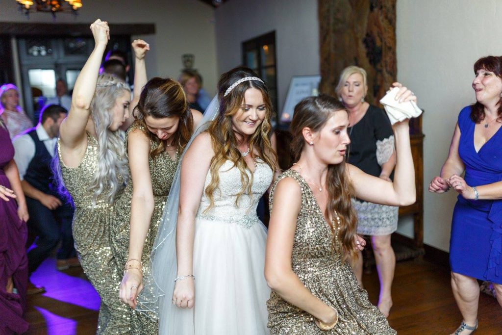bride with headband and veil dancing with bridesmaids in gold dresses