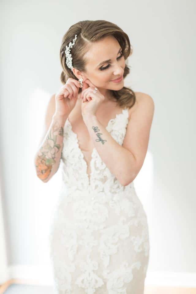 bride smiling and fixing her earrings while in her wedding dress by Beauté Spécialé