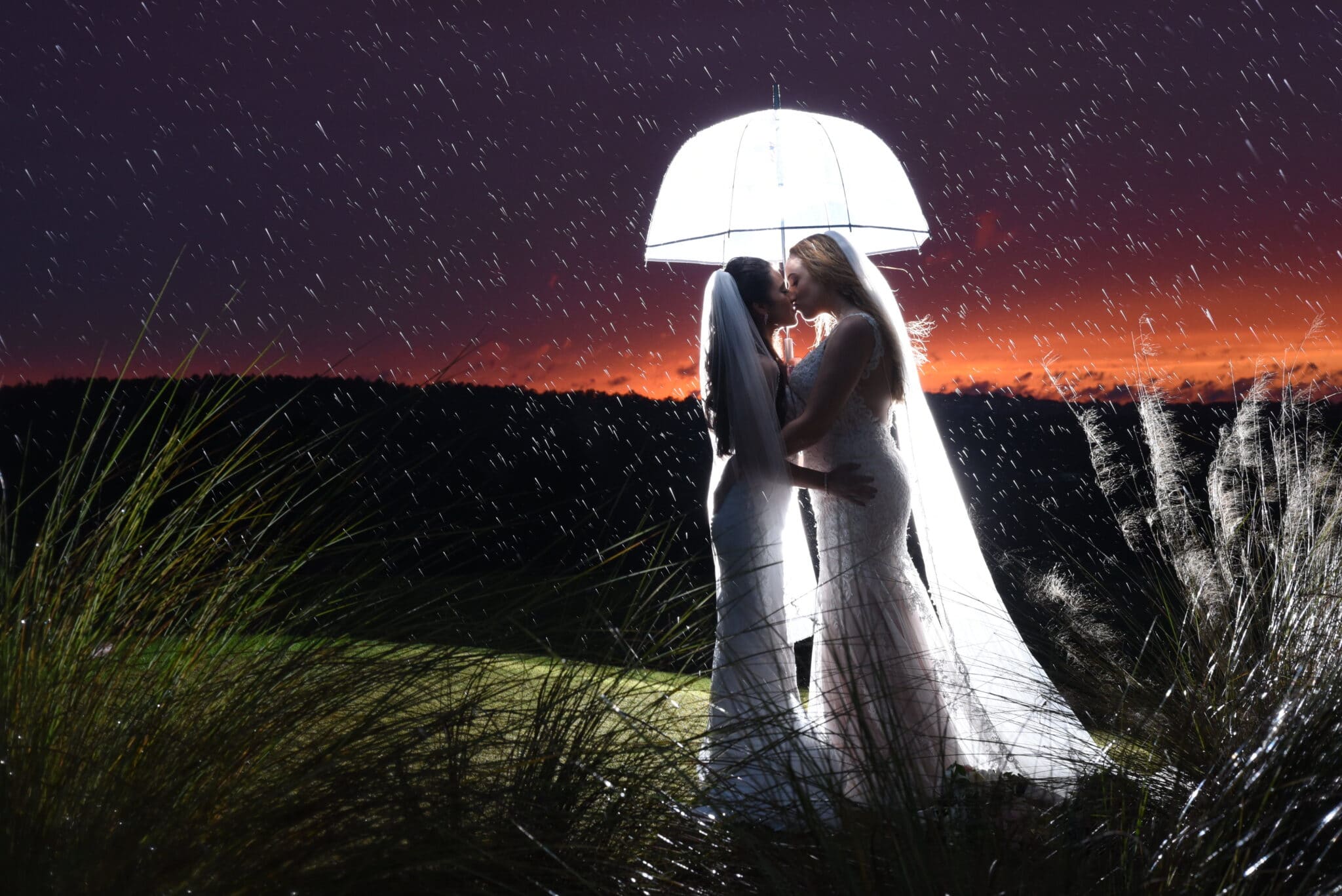 Anna Christine Events- brides kissing under white lit umbrella at sunset