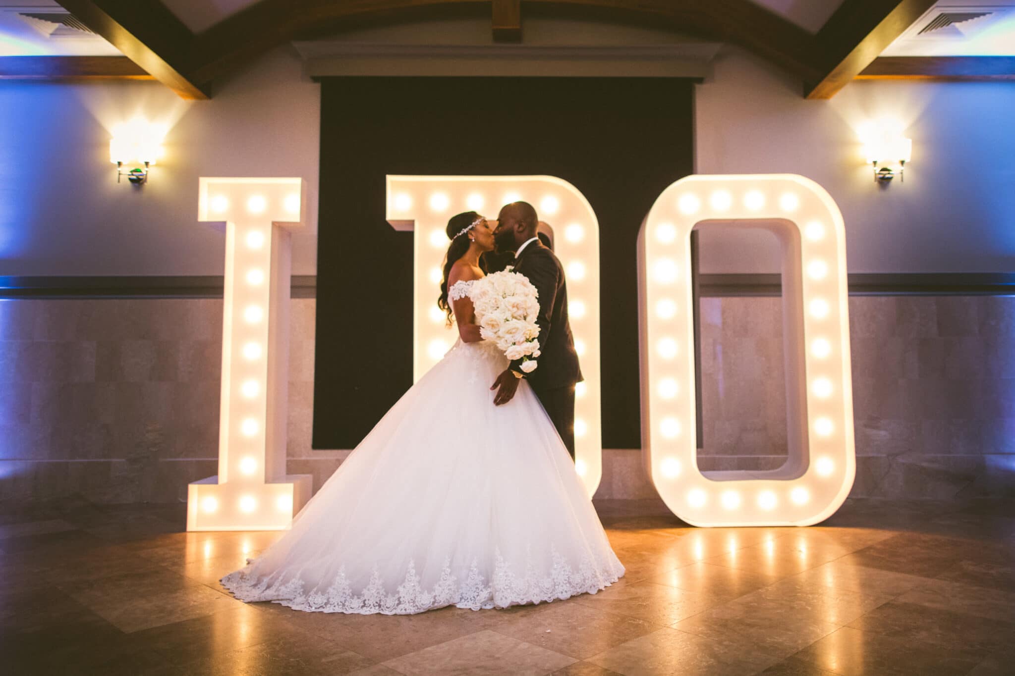 Anna Christine Events, bride & groom kissing in front of I DO light sign