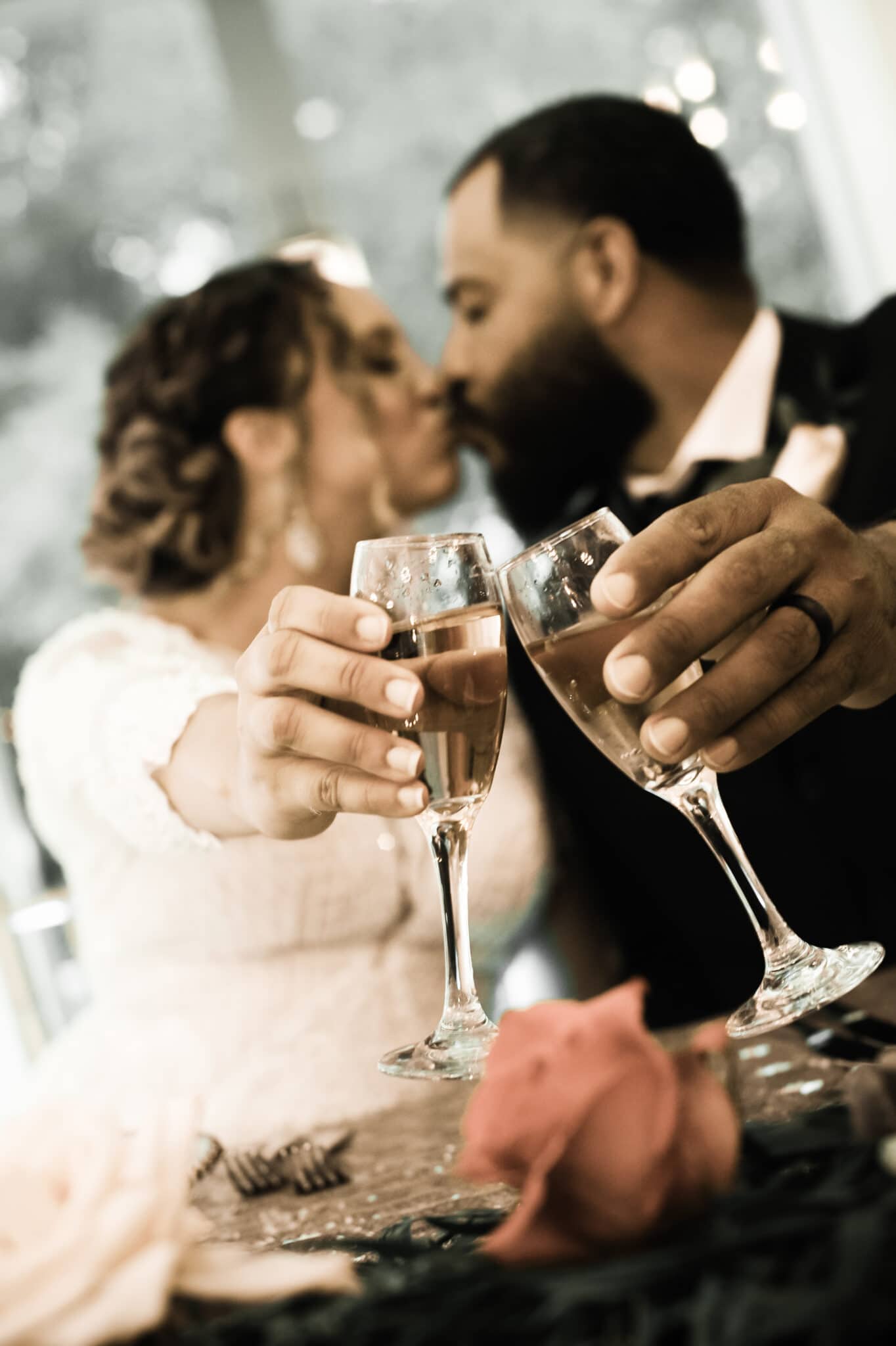 close up of champagne glasses with bride & groom kissing in background
