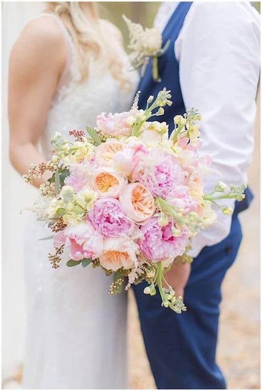Lowe and Behold bride and groom holding flower bouquet featuring pinks and light oranges