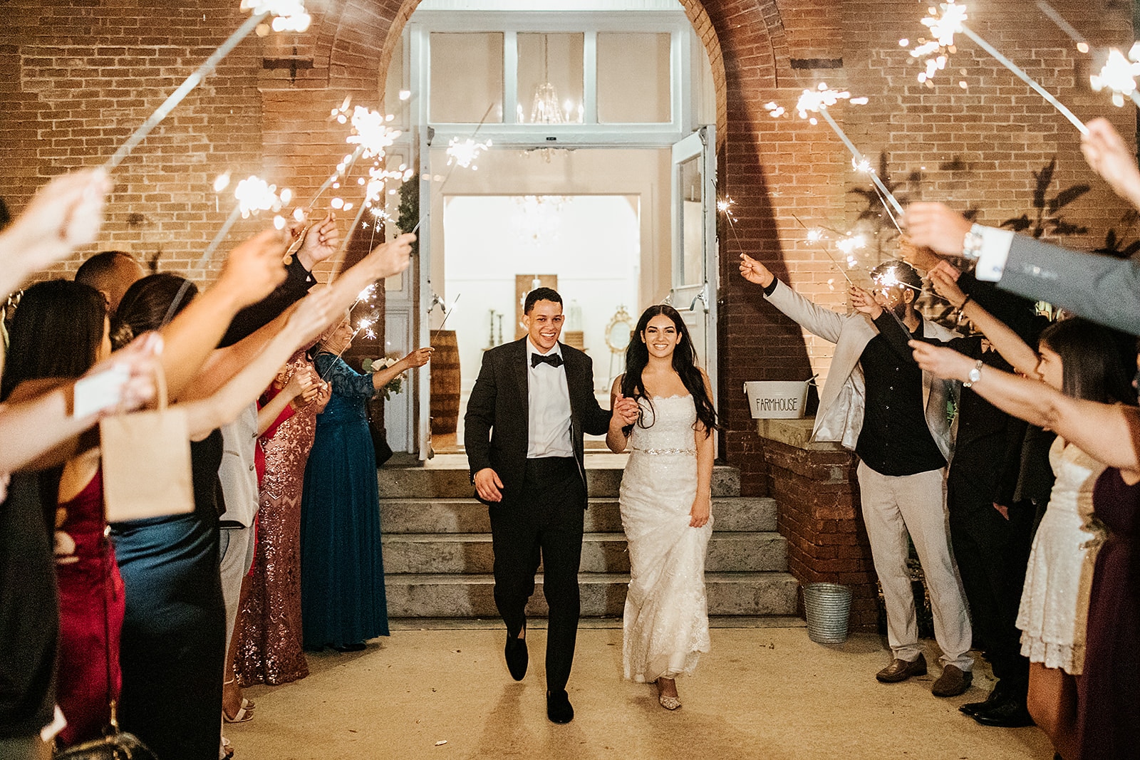 bride and groom walking outside with guest holding sparklers